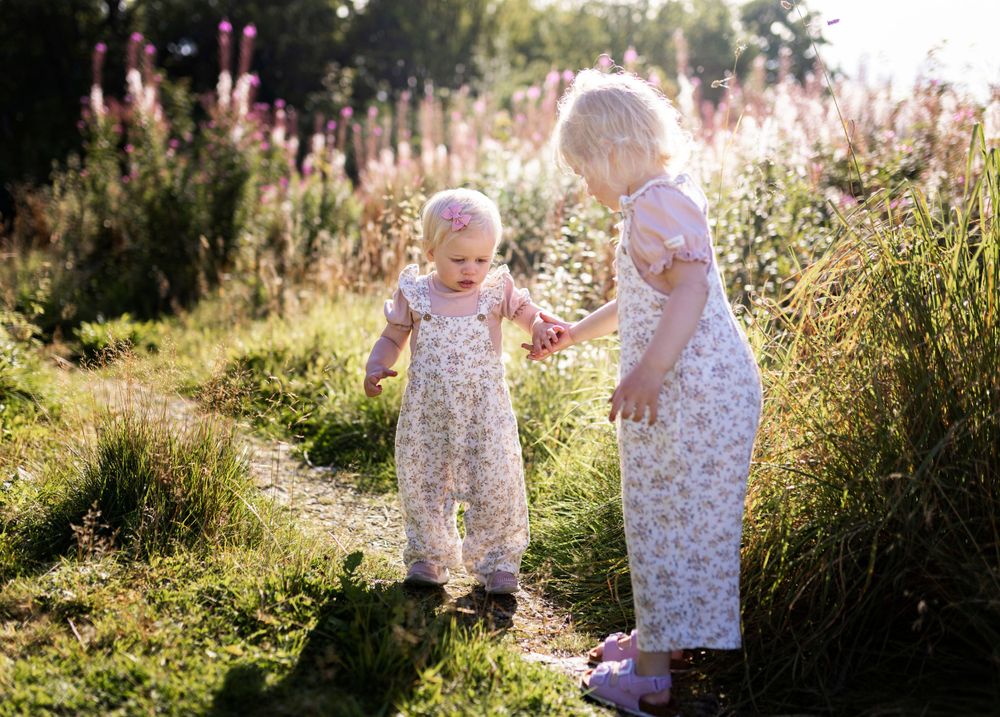Two small figures in floral dresses sharing a sunny moment among wildflowers.