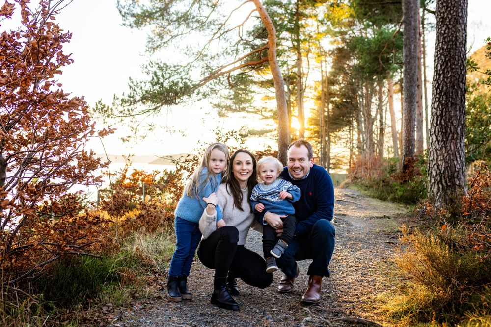Family group photo on wooded path during golden hour sunset.