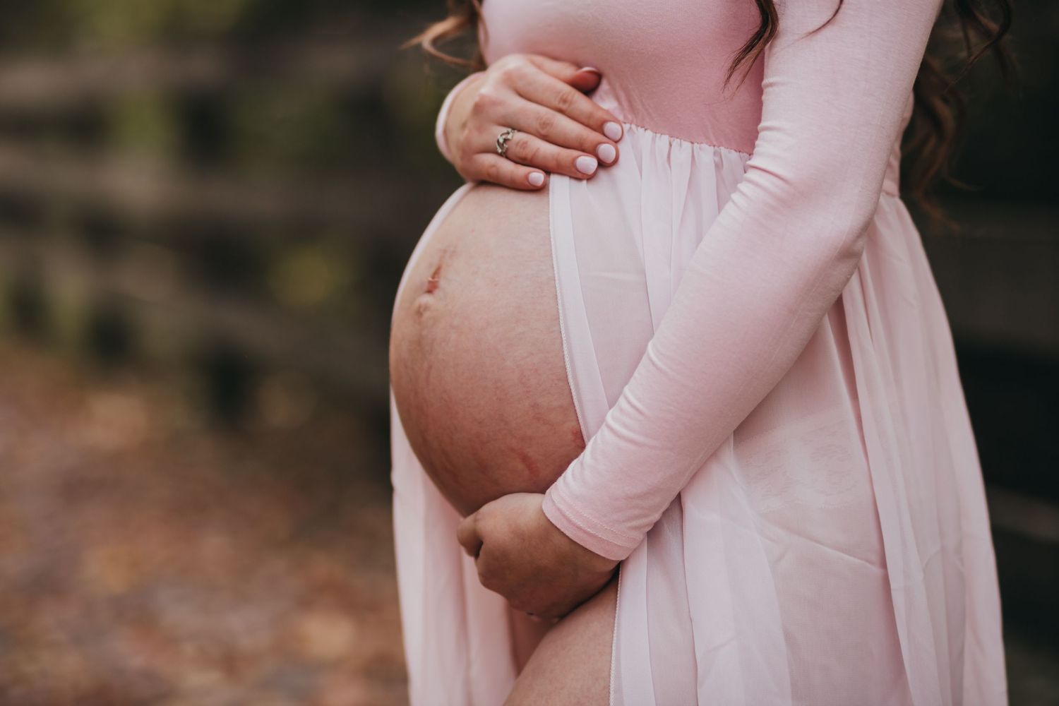 Expecting mother in pink dress cradles her baby bump during maternity photoshoot.