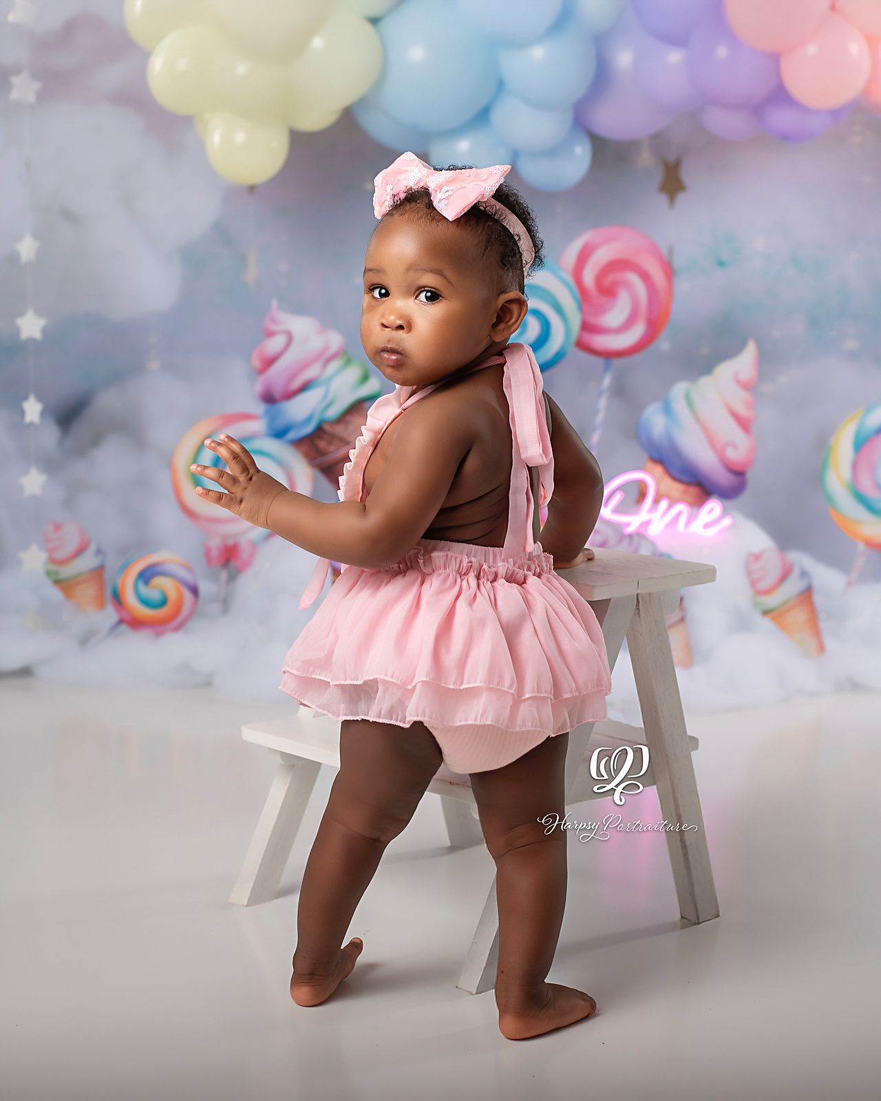 Sassy birthday girl wearing pink dress Cake Smash photos; pastel balloon arch, clouds, lollipops; baby photographer; Lexington, SC studio
