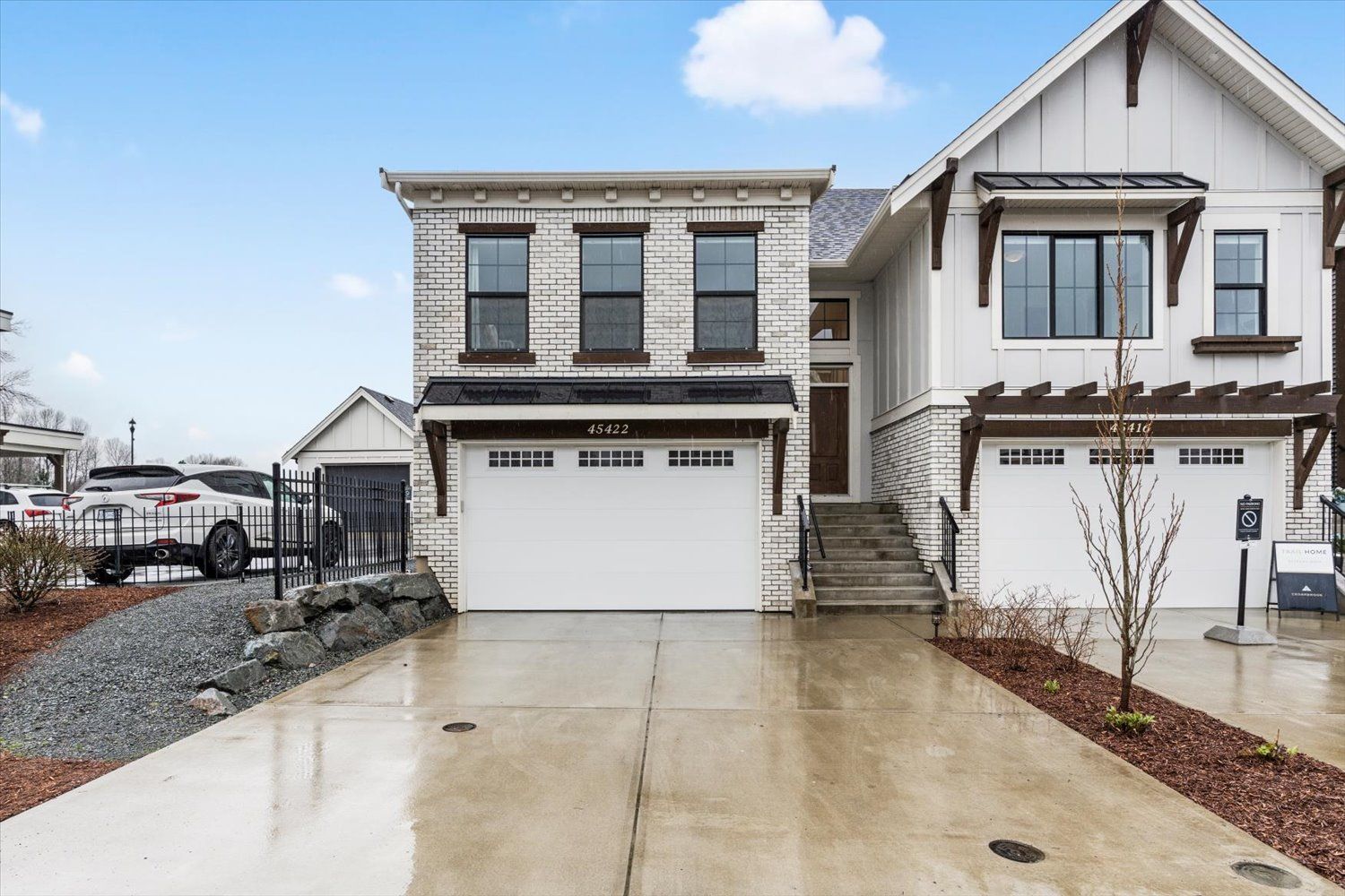 Modern two-story home with white exterior, double garage doors and concrete driveway on a wet or rainy day.