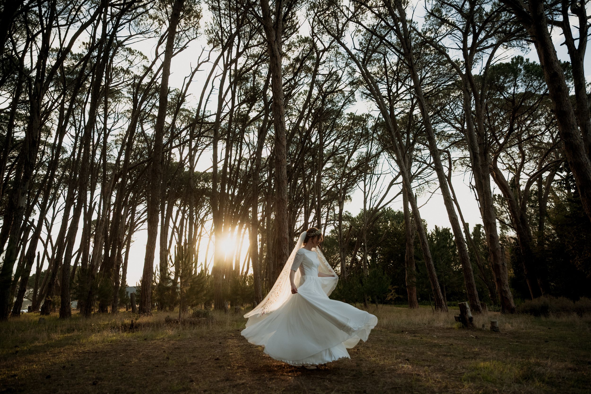A flowing white wedding dress twirls dramatically in a sunlit forest setting during golden hour.