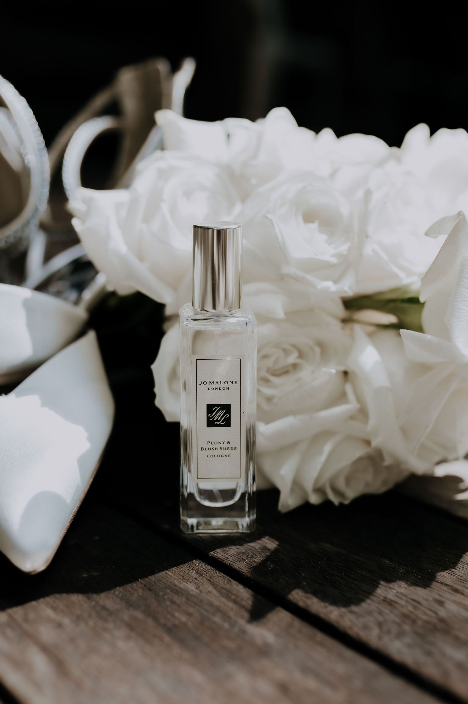 Perfume bottle displayed with white roses on rustic wooden surface.