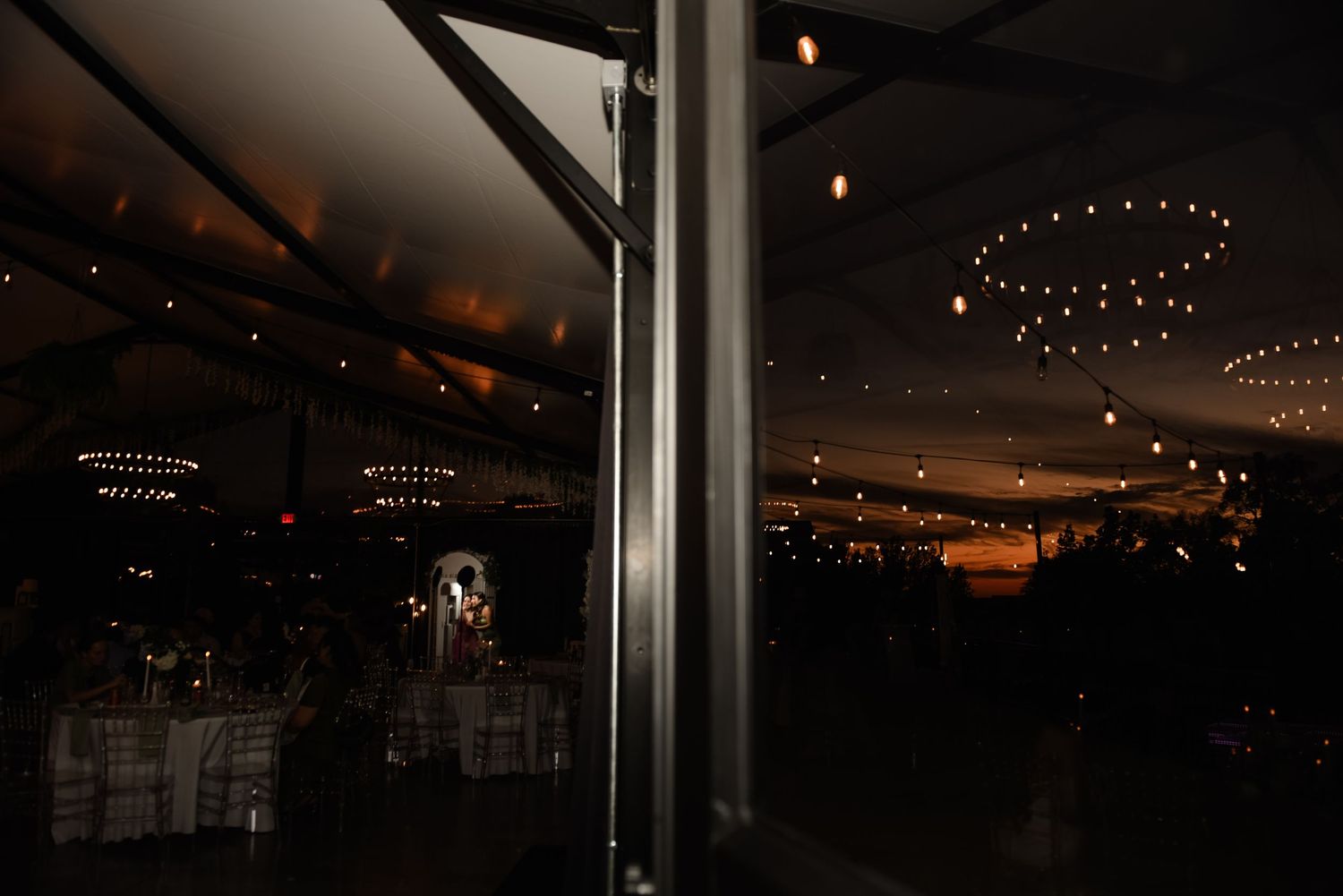 Two beautiful brides in an outdoor LGBTQ wedding celebration dancing closely together under a canopy of string lights at dusk in Dallas, TX