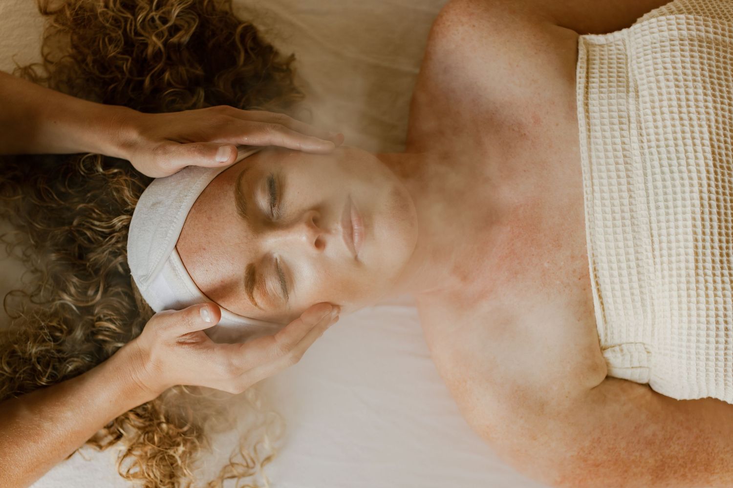 Woman receiving a relaxing facial massage at a spa, with eyes closed and a white headband.