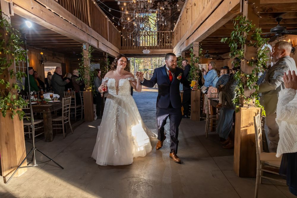 Newlyweds making grand entrance into rustic barn wedding reception with string lights.