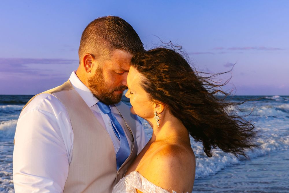 Romantic couple shares an intimate moment on a windy beach at dusk by the ocean.