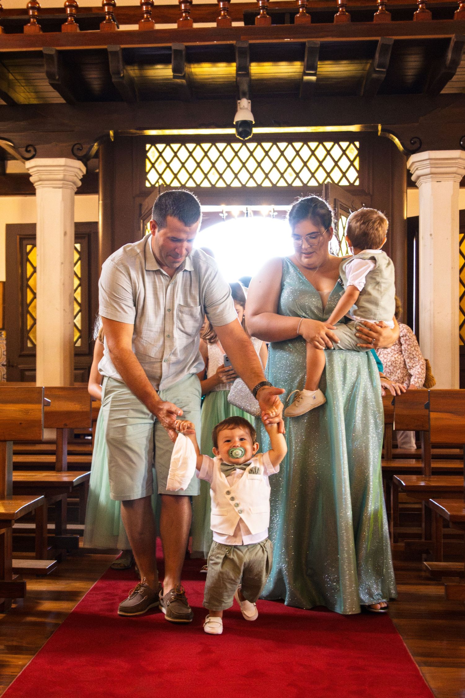 Group in white and mint green attire gathered at church ceremony with ornate wooden columns.