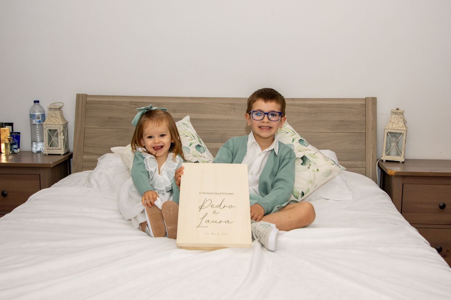 Family lying together on a white bed with wooden headboard.