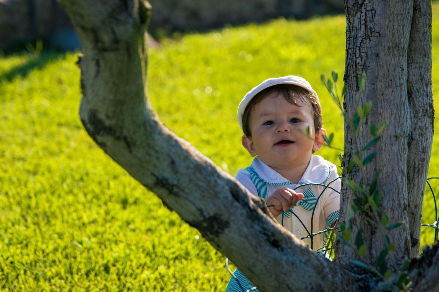 Child playing in bright green grass on a sunny day with trees in the background.