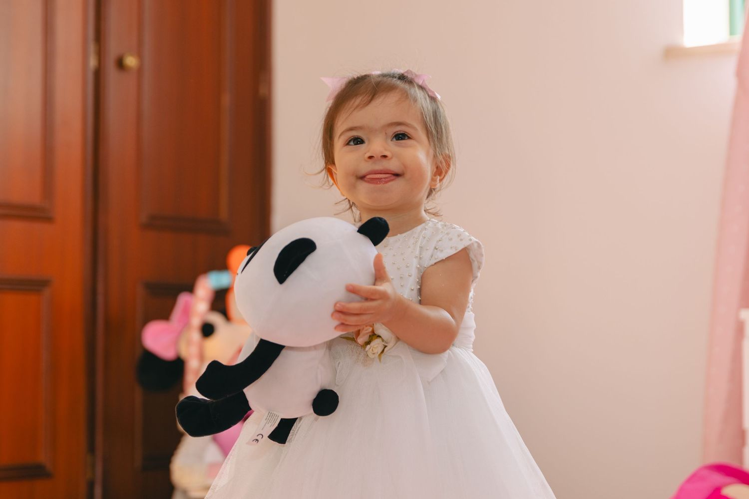 Two young children playing with stuffed panda bears in front of a pink wall.