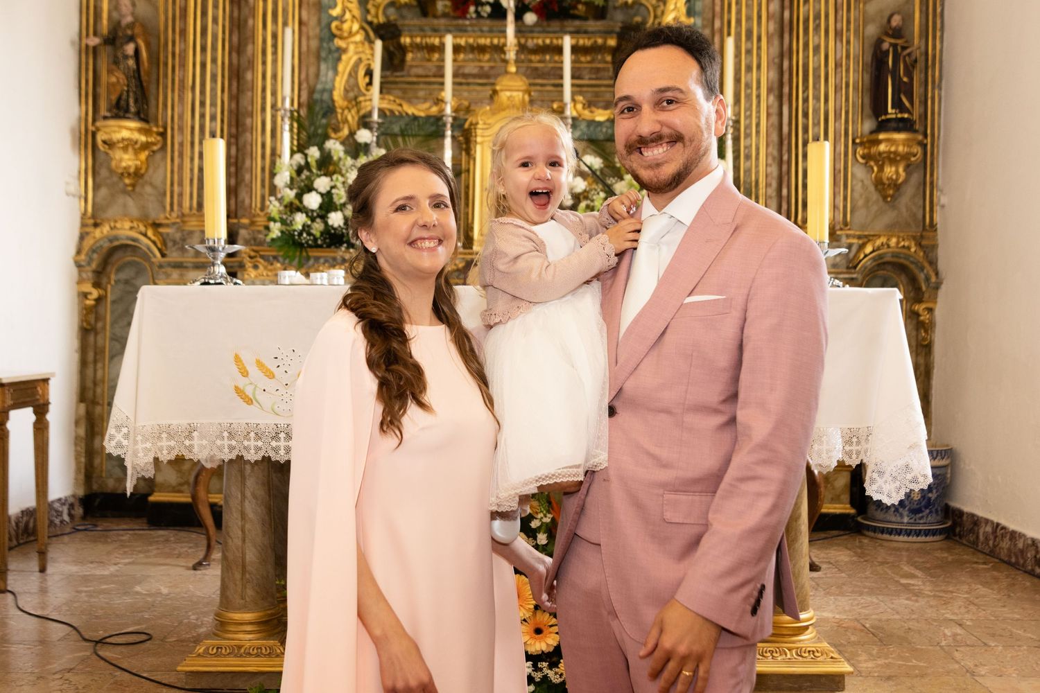 A family celebration portrait in an ornate church with gilded altar and white floral decorations.