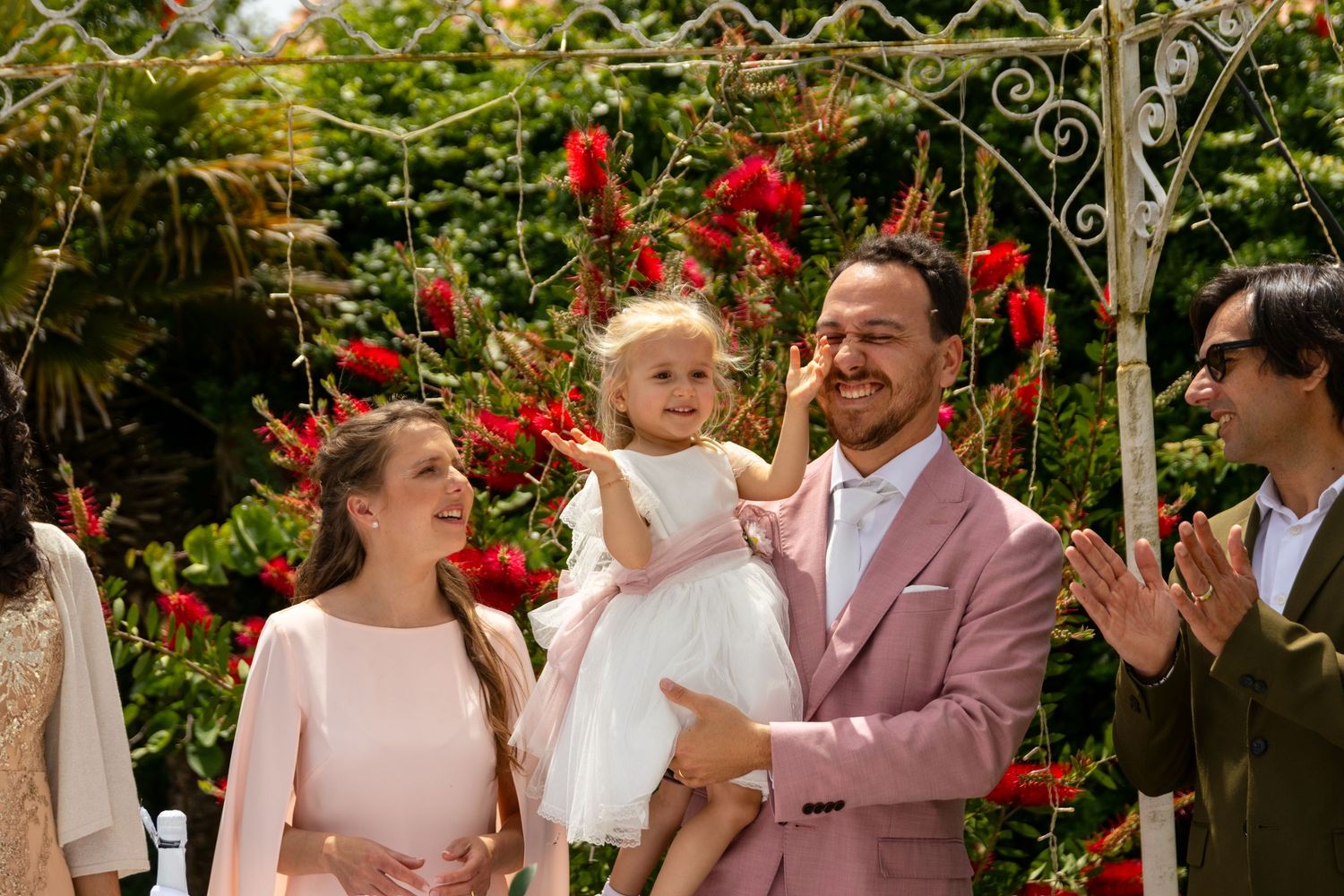 A joyful family moment in a garden with blooming red flowers and decorative ironwork.