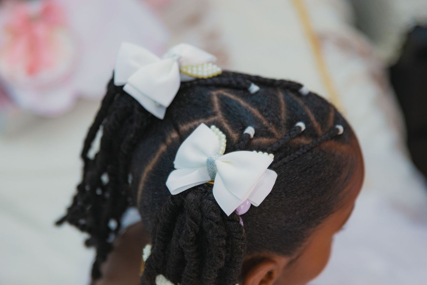 Close-up of intricate black braided hairstyle decorated with small white bows.