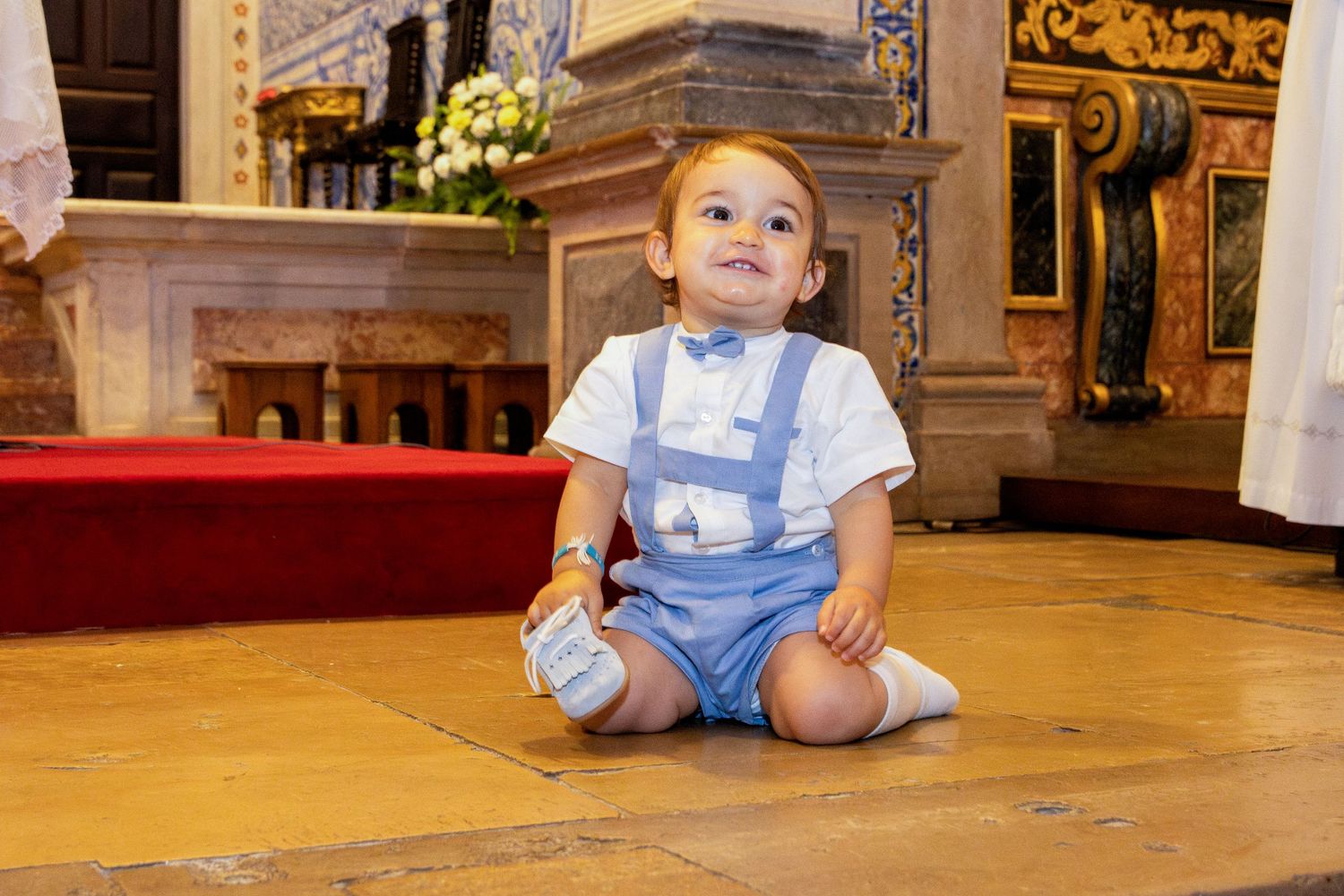 Baby wearing blue and white outfit sits on ornate church floor.