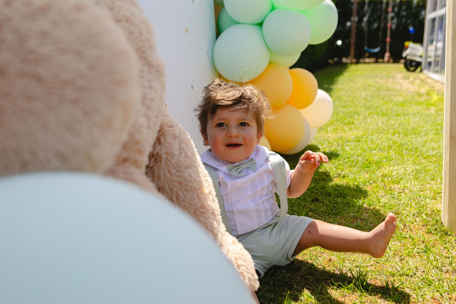 Toddler in purple dress sitting by colorful balloons in garden.