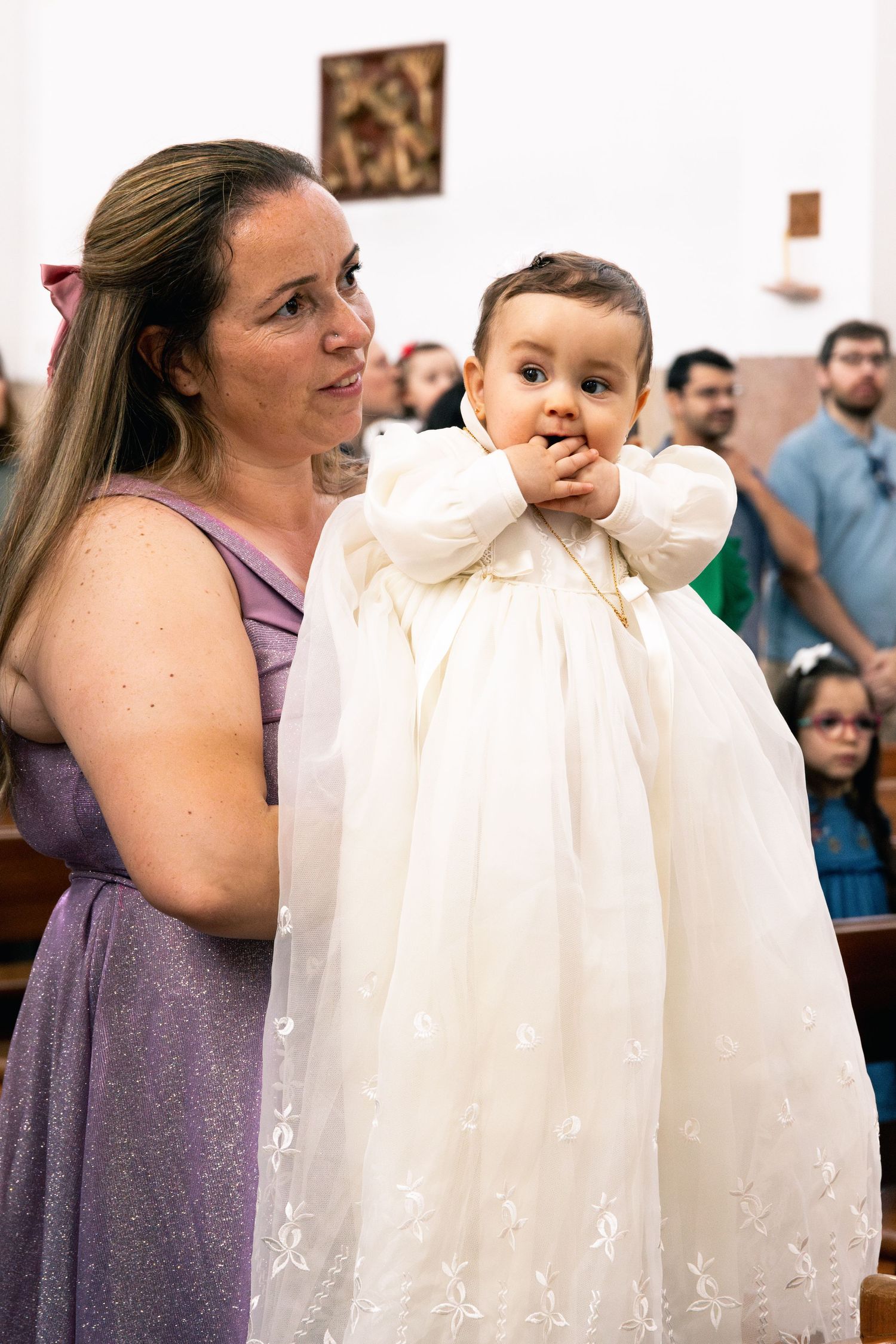 A baptism ceremony in progress showing a white christening gown in a church setting.