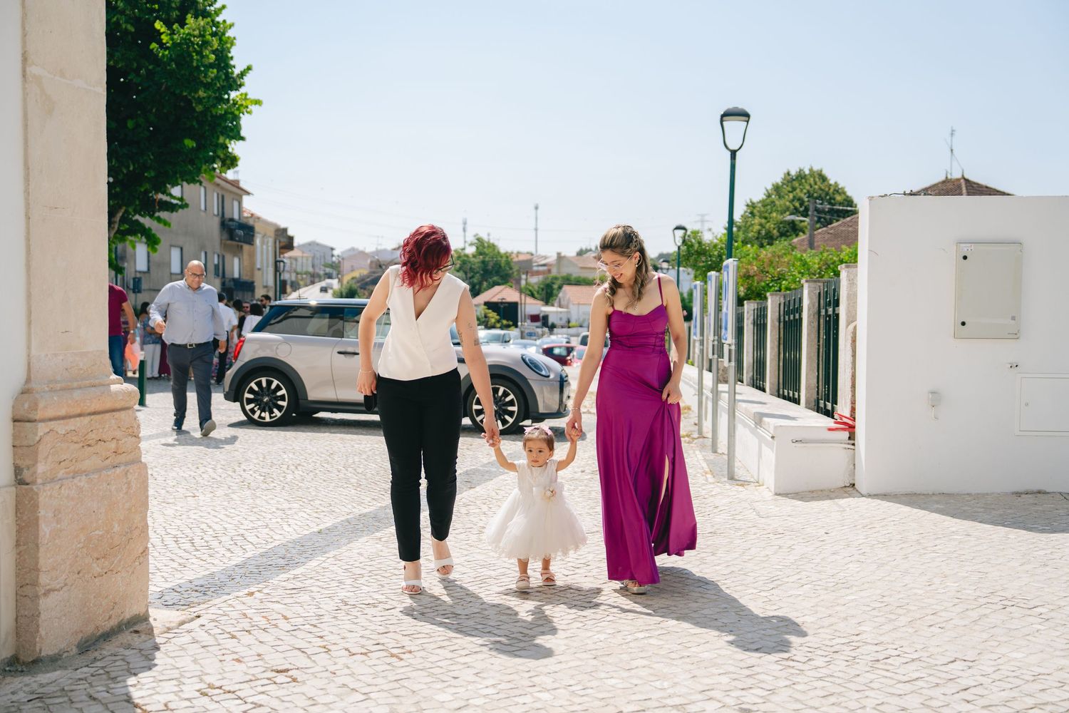 Wedding party members walk down a stone pathway at a seaside venue on a sunny summer day.