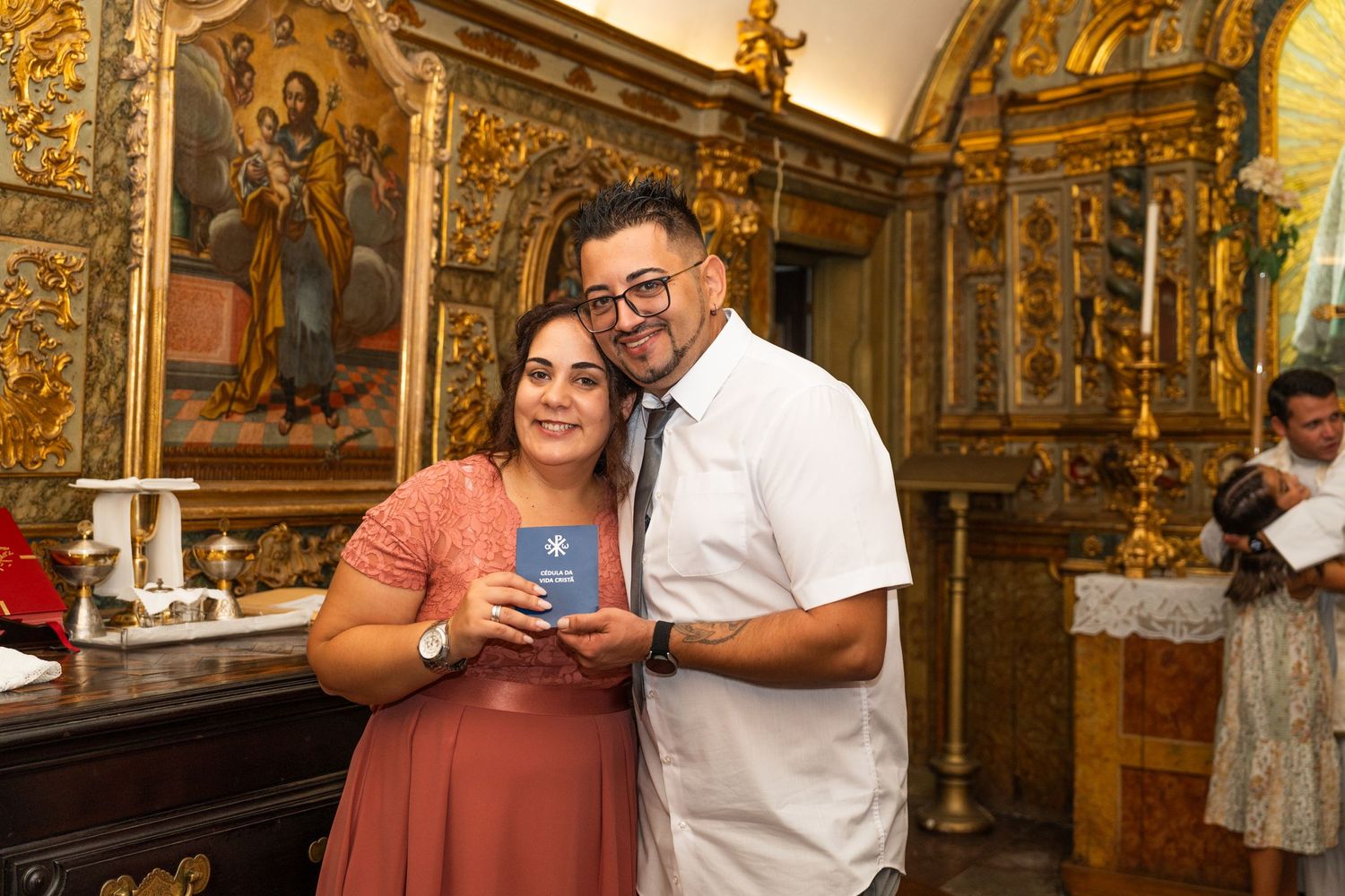A couple poses with a blue item inside an ornate church with golden religious iconography in the background.