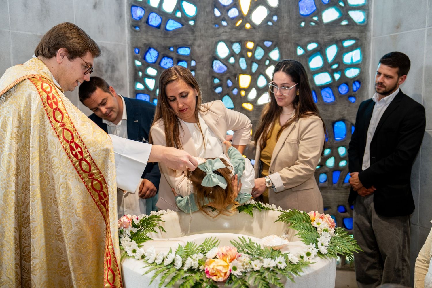 Religious ceremony taking place in front of stained glass windows with colorful lighting.