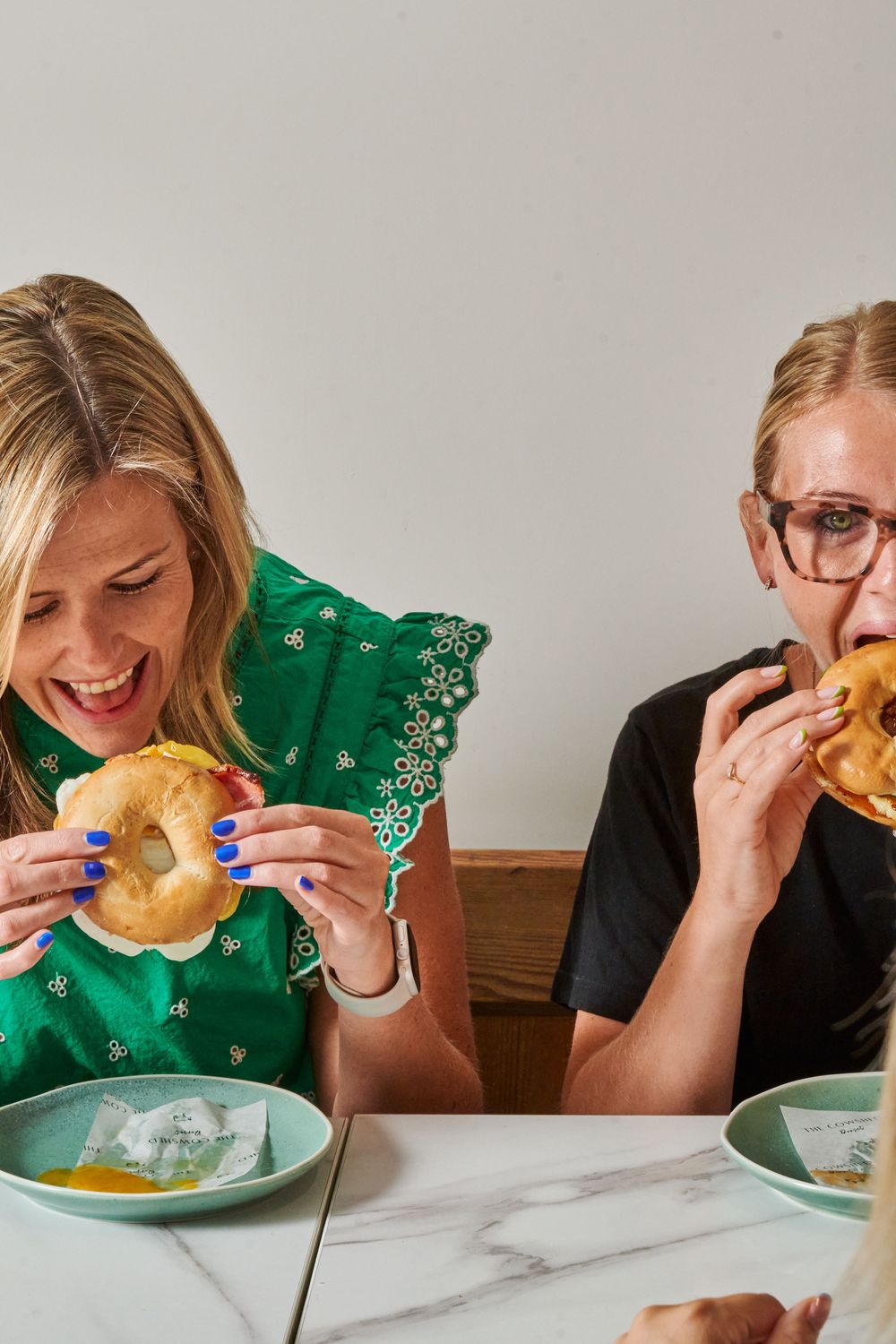 two friends taking bites from a bagel on a white plate against a light background  Aggie Bea Commercial food and drink photographer