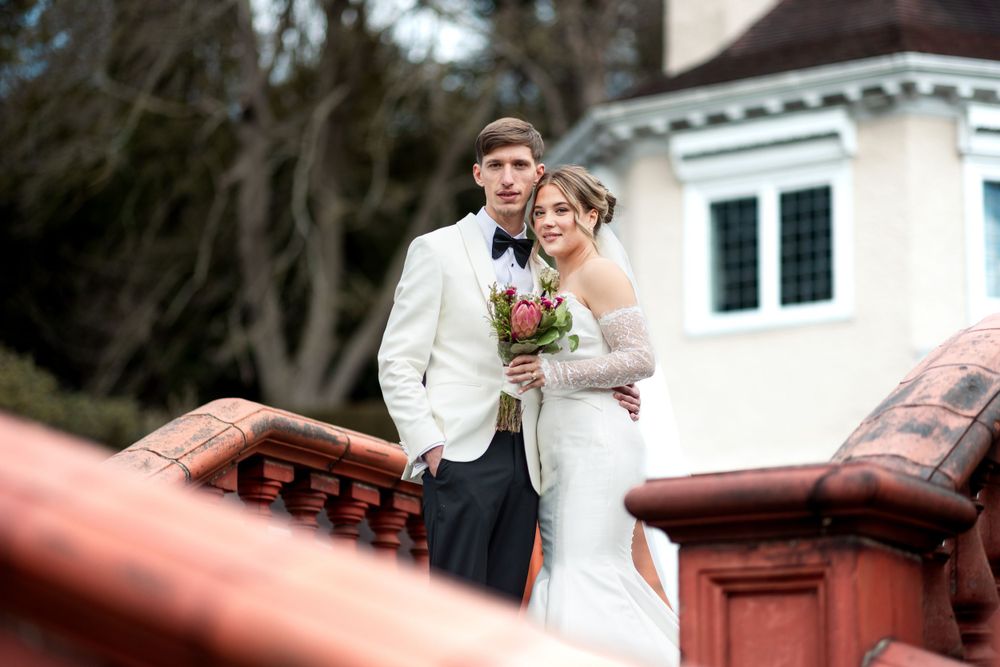 A bride and groom stand together on stone steps with a white building in the background on their wedding day.