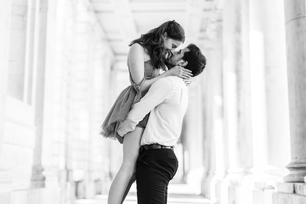 A romantic black and white portrait of a couple embracing against a backdrop of classical columns.