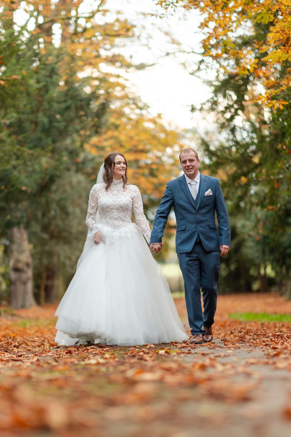 A couple walking hand in hand along an autumn path covered in fallen orange leaves.
