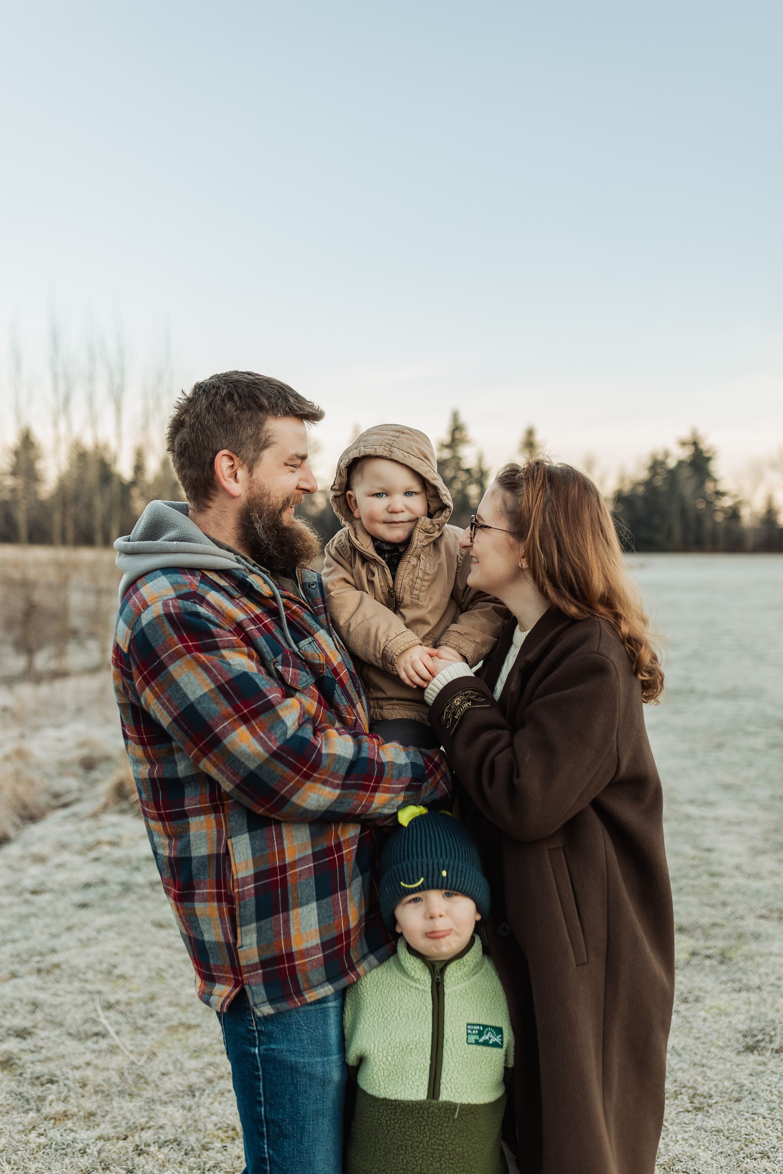 A family in winter clothing shares tender moments together in a frosty outdoor setting at sunrise.