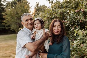 Happy family portrait outdoors with toddler among green foliage.