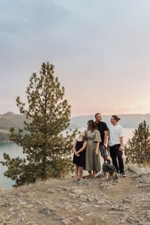 A group enjoying the scenic mountain view while standing on a cliff overlooking a lake at sunset.