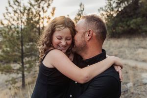 A tender embrace between a couple wearing black clothing against a natural outdoor backdrop at sunset.