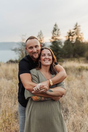 A joyful couple embracing in a field with mountains and pine trees in the background at golden hour.