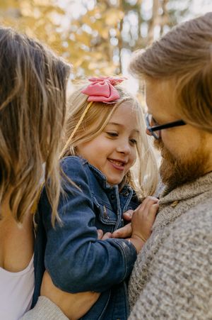 Intimate family moment captured in warm sunlight with autumn leaves in the background.