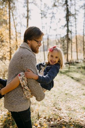 Playful moment in an autumn forest with someone carrying a child wearing a denim jacket.