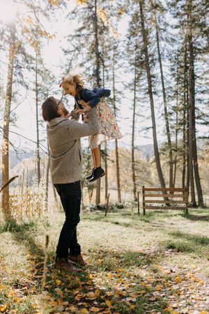 Joyful moment in a fall forest with someone lifting a child high in the air.