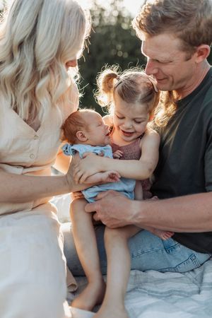 Family shares tender moment with newborn baby and toddler in sunset light.
