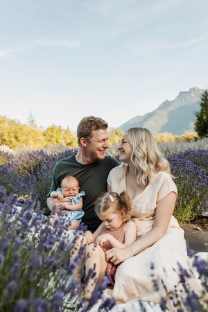 Family sitting in lavender field with mountain backdrop during summer photoshoot.