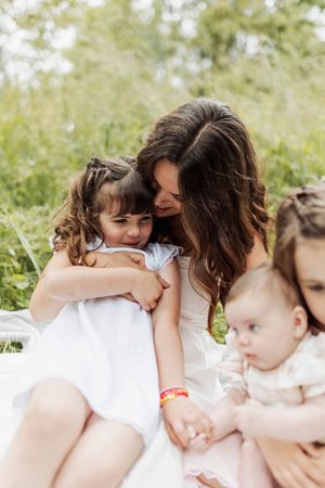 Tender moment between mother and children sitting in sunny meadow.
