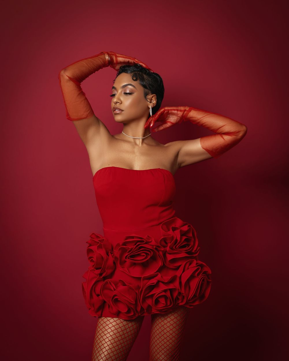 A woman in a red strapless floral mini dress and red gloves poses dynamically against a red backdrop.