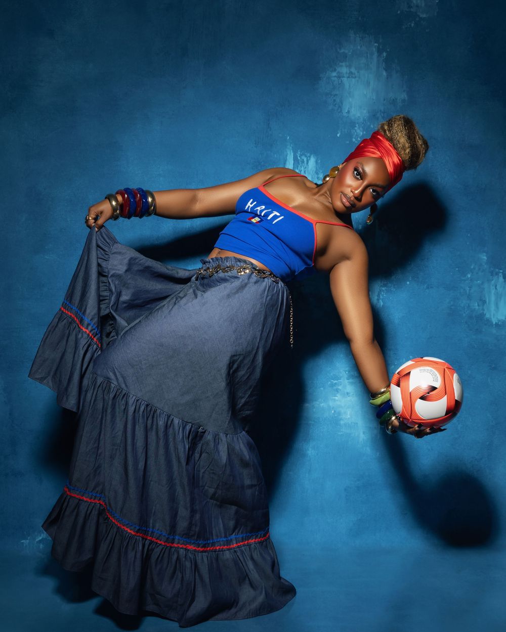 Woman in blue Haiti top and denim skirt reclines gracefully holding Adidas soccer ball.