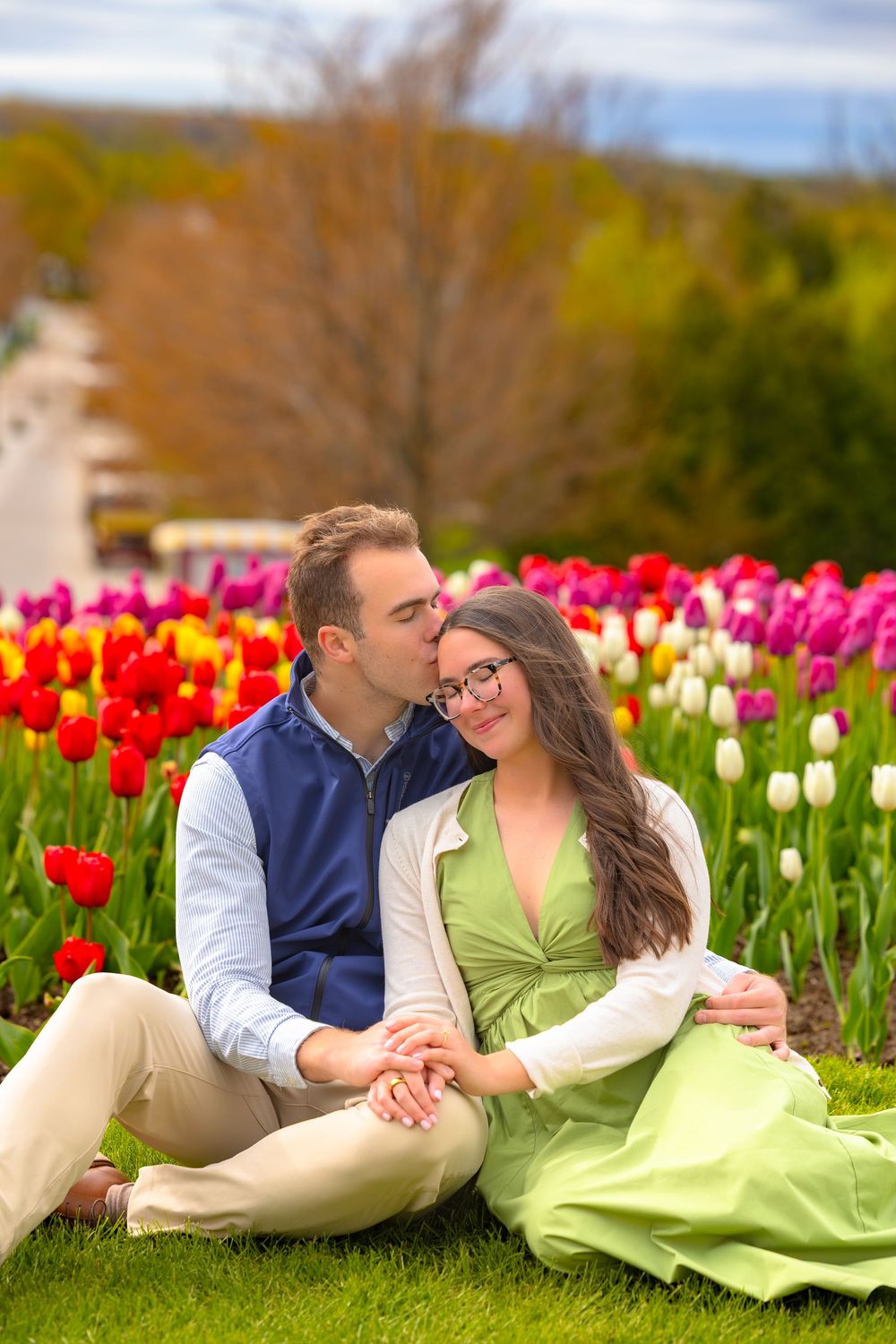A couple in coordinated outfits share romantic moments among vibrant red and pink tulips in a spring garden.