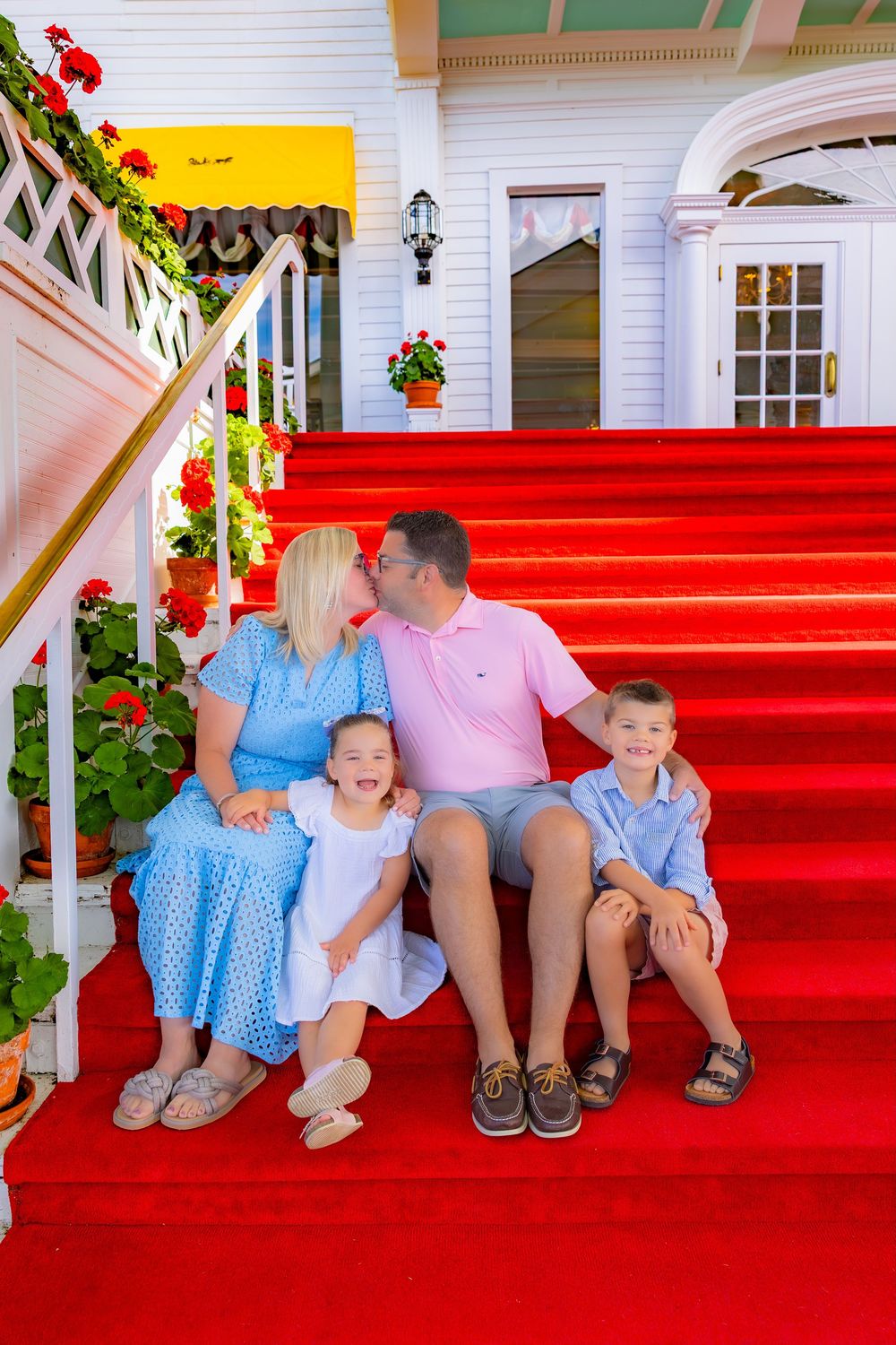 Family sitting together on bright red carpeted steps decorated with festive greenery and red flowers.