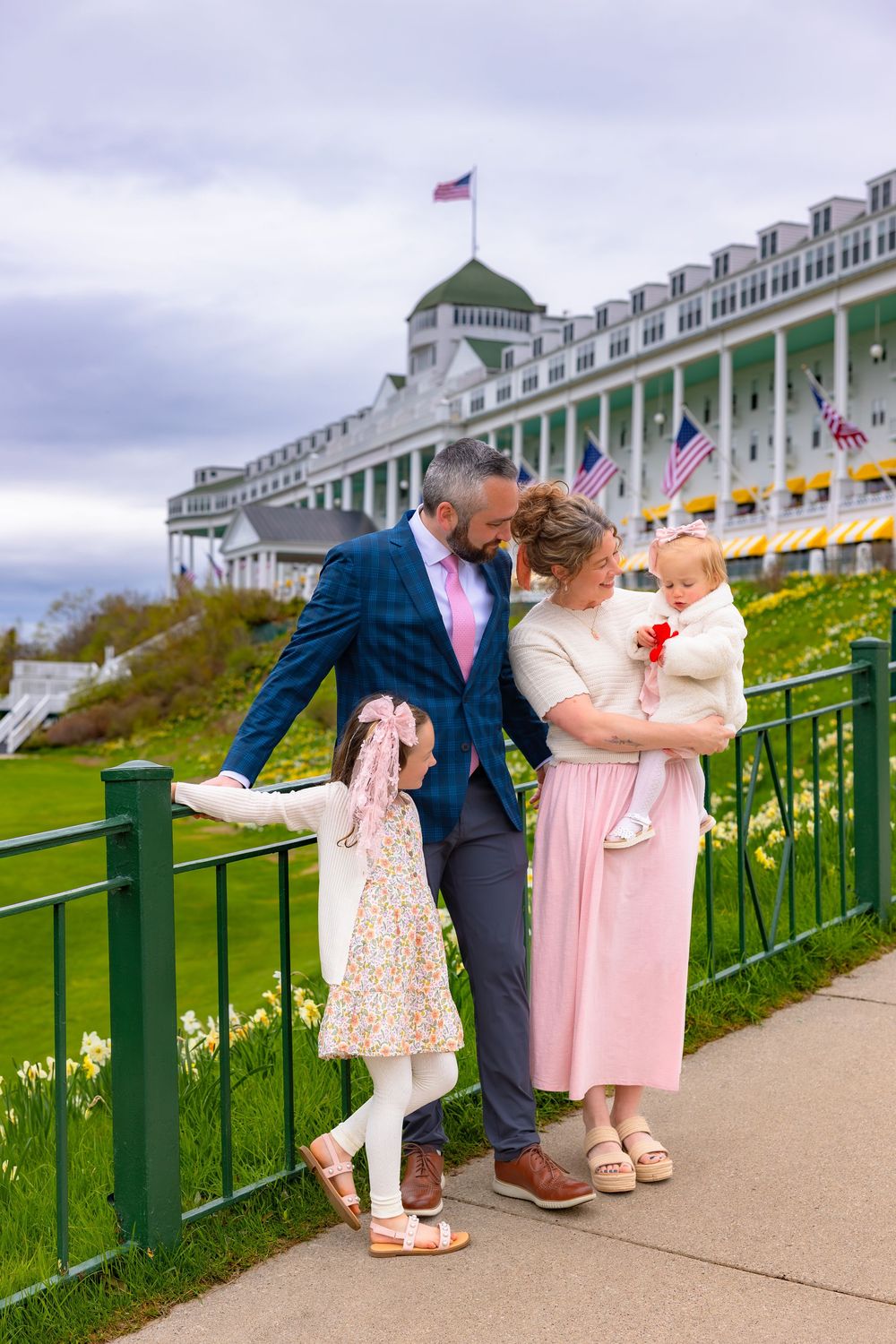 A family in coordinated pink and blue outfits poses together on the Grand Hotel porch on Mackinac Island.