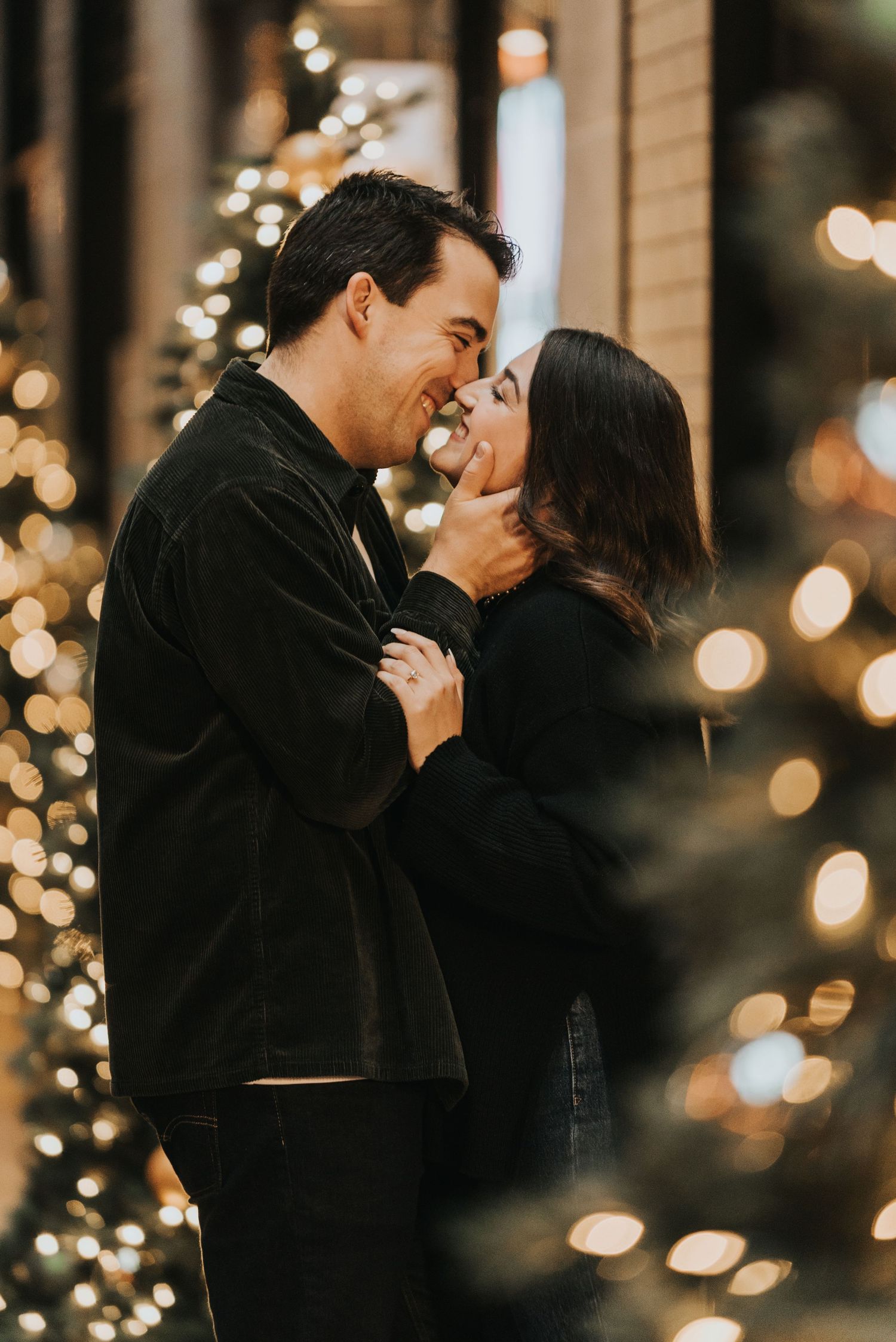 Romantic couple sharing a tender kiss in front of twinkling holiday lights creating a magical nighttime ambiance.