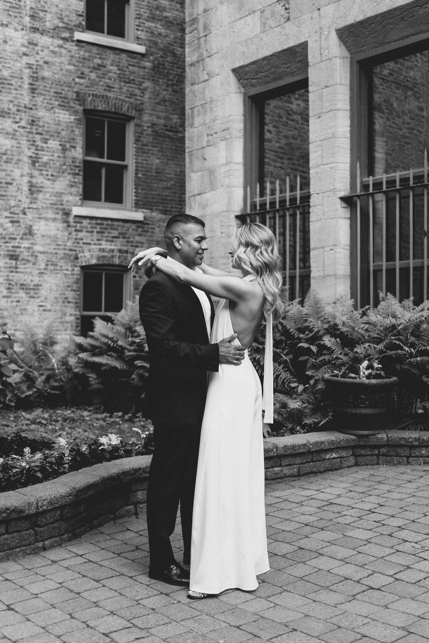 Romantic sequence of black and white photos showing a couple dancing and embracing in front of a brick building.