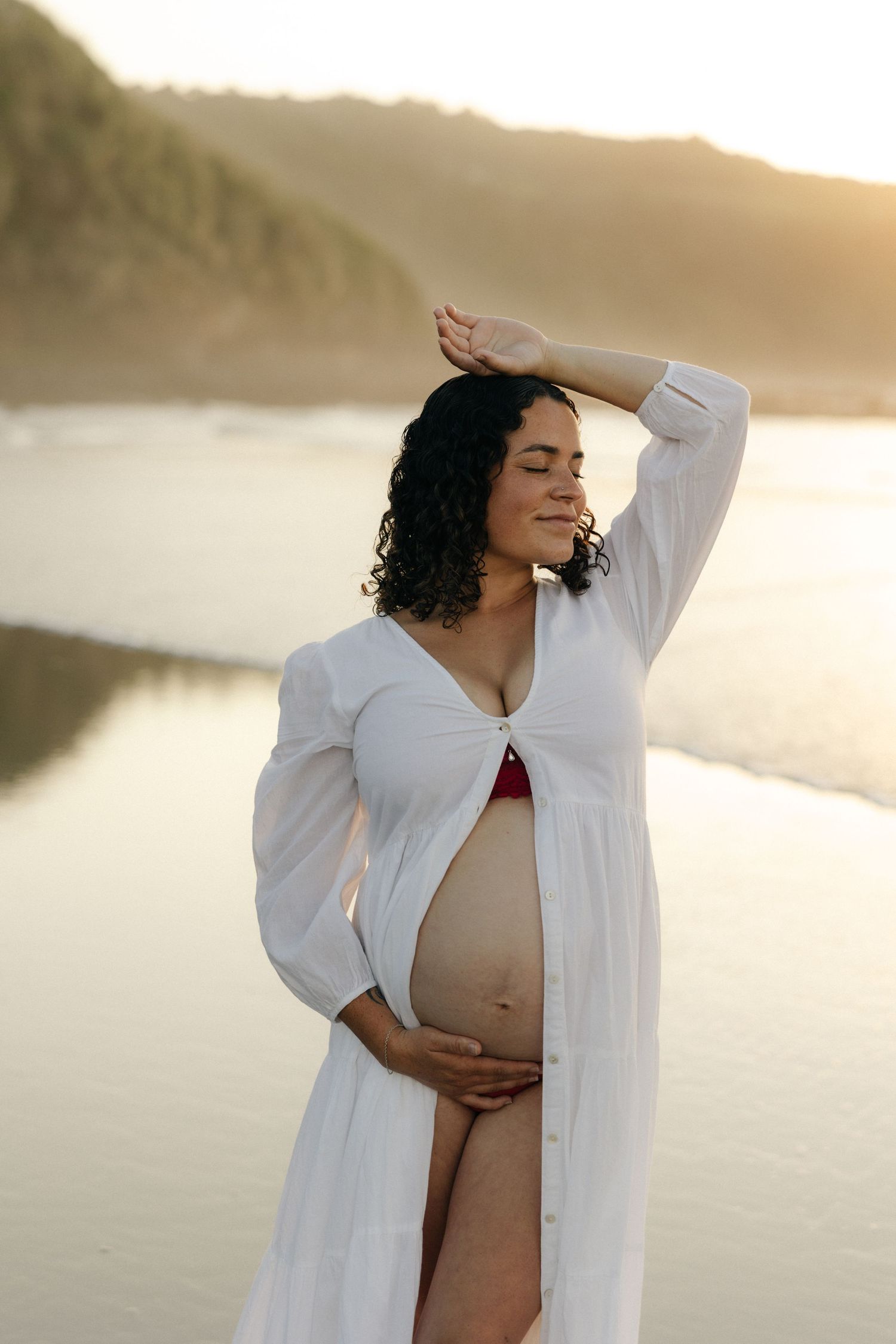 A maternity photoshoot in a serene forest setting with soft natural lighting and flowing white lace dress.