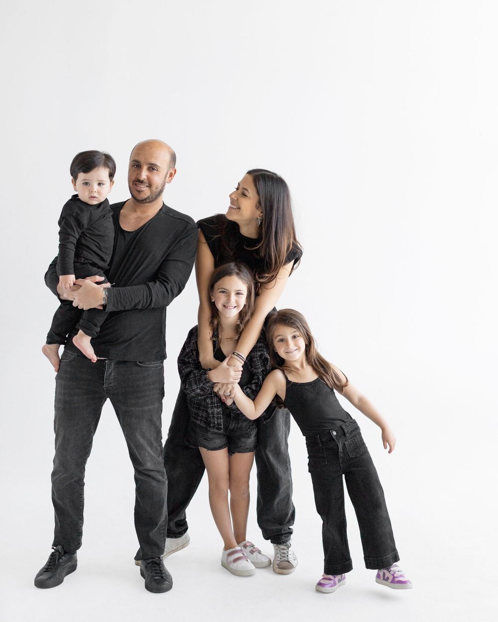 Family of five in matching black outfits posing together against white background in studio portrait.