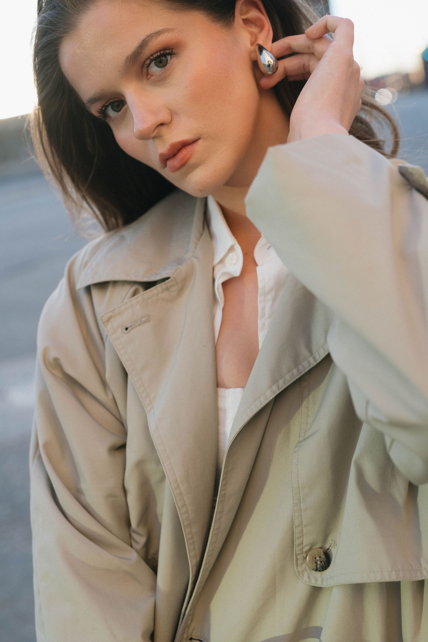 Fashion model wearing a beige trench coat and white top adjusts pearl earring in outdoor portrait setting.

Saskatoon Portrait Photographer