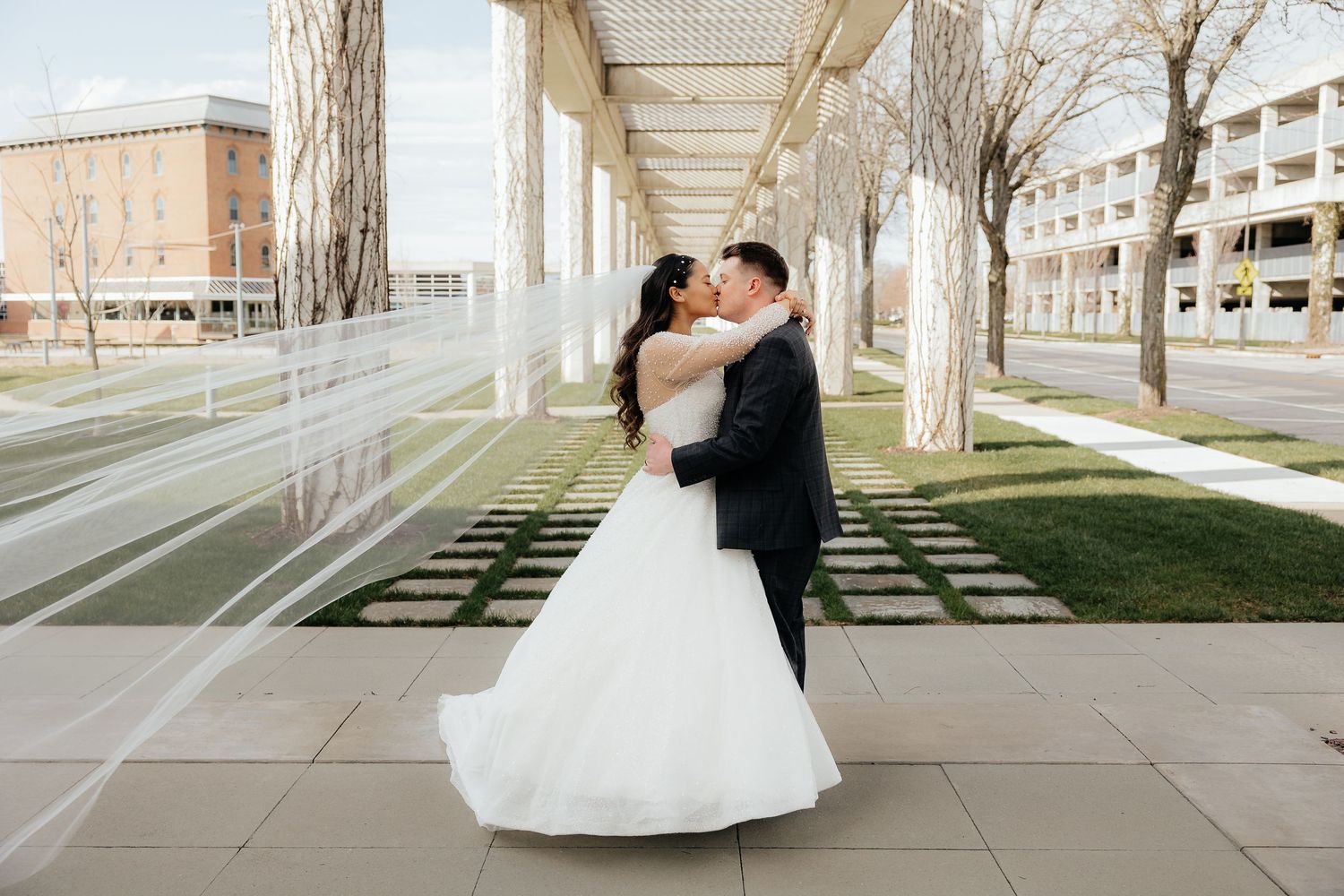 Wedding couple embracing under modern architectural columns outdoors.